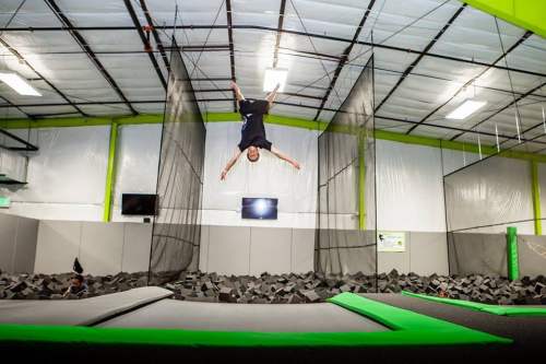 A person performs a backflip above a trampoline, surrounded by foam blocks in a trampoline park.