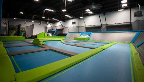 A spacious indoor trampoline park featuring multiple trampolines with green and blue padding.