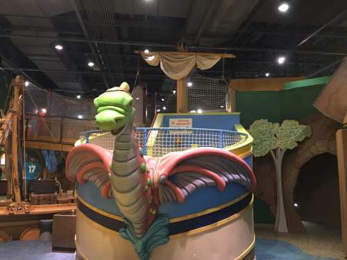 Colorful dragon figure on a play structure, with a ship's sail and trees in a children's play area.