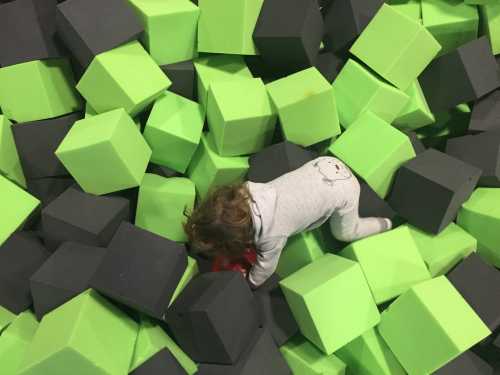 A child in pajamas crawls through a colorful foam pit filled with green and gray blocks.