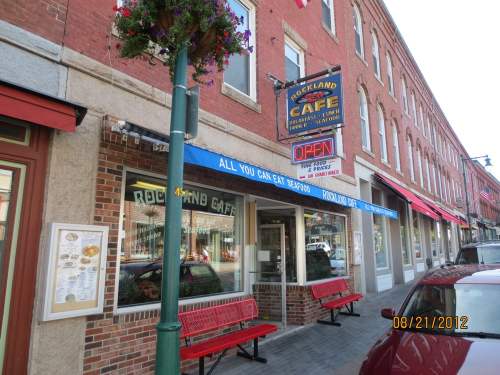 A street view of Rockland Café with outdoor seating, colorful signage, and a brick building facade.