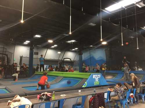 A lively indoor trampoline park with people jumping, playing, and enjoying various activities. Bright colors and seating visible.