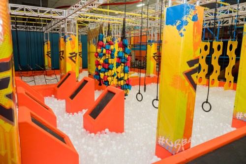 Colorful indoor obstacle course featuring climbing walls, swings, and a ball pit. Fun and vibrant play area.