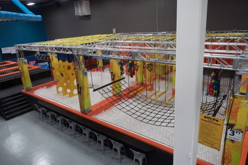 A colorful indoor play area featuring trampolines, climbing structures, and safety nets.
