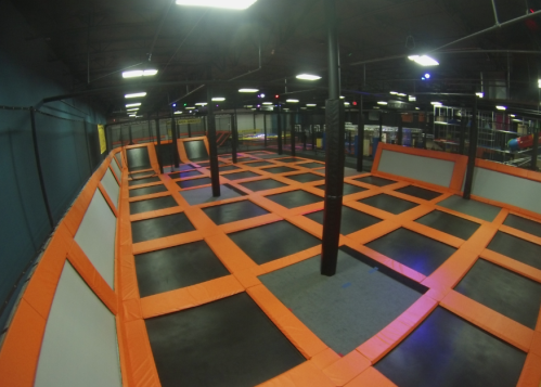 A spacious indoor trampoline park with orange trampolines and black flooring, featuring multiple jumping areas.