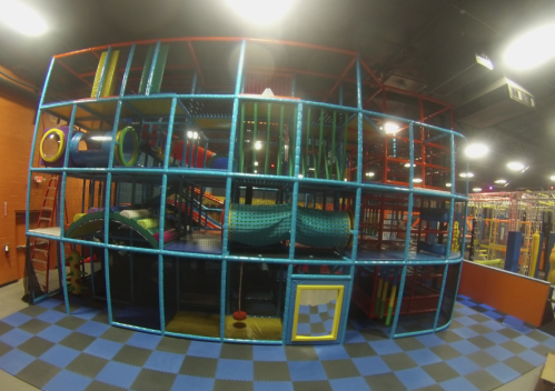 Colorful indoor playground structure with slides, tunnels, and climbing areas, surrounded by blue and black checkered flooring.