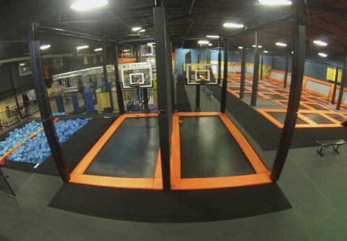 A vibrant indoor trampoline park featuring basketball hoops, foam pits, and multiple jumping areas.