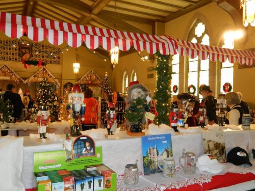 A festive market scene with decorated tables, nutcracker figures, small trees, and holiday decorations in a church setting.