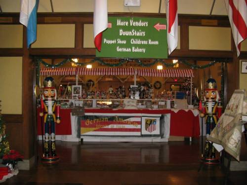 Entrance to a festive market with nutcracker decorations, signs for vendors, and a German bakery.