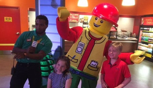 A LEGO character poses with a man and two children in a colorful indoor setting.