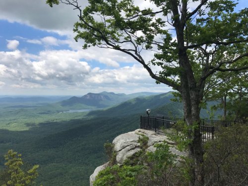 A scenic view from a rocky overlook, featuring lush green mountains and a cloudy sky in the background.