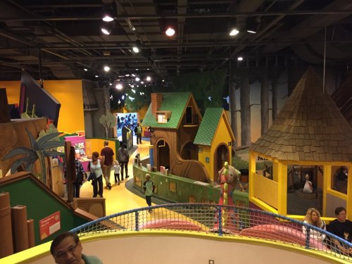 Colorful indoor play area with various structures, children playing, and adults supervising in a vibrant, whimsical setting.