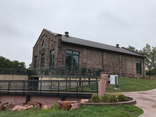 Historic stone building with large windows, set on a grassy area with a pathway in front, under a cloudy sky.