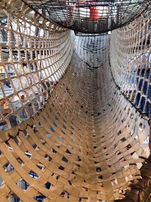 A large, suspended net structure in a play area, creating a tunnel-like space for climbing and exploration.