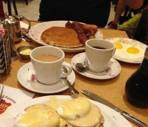 A table set with breakfast: pancakes, bacon, eggs, coffee, and eggs Benedict.