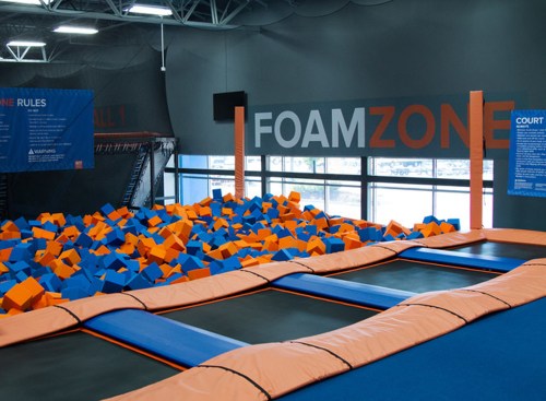A trampoline area with a foam pit filled with orange and blue blocks, surrounded by safety rules signage.