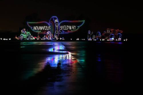 Colorful holiday lights display at the Indianapolis Motor Speedway, reflecting on a wet surface at night.