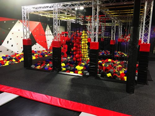 Indoor adventure park featuring climbing walls, foam pits, and obstacle courses in vibrant colors.
