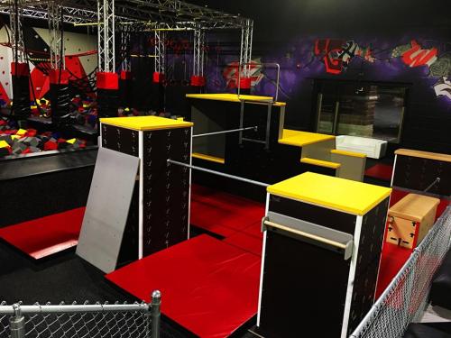 An indoor obstacle course featuring various platforms, foam pits, and climbing structures in vibrant colors.