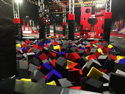 A colorful foam pit filled with black, red, yellow, and blue blocks in a trampoline park setting.