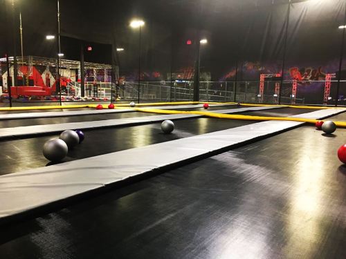 An indoor trampoline park featuring multiple trampolines and colorful balls scattered across the floor.