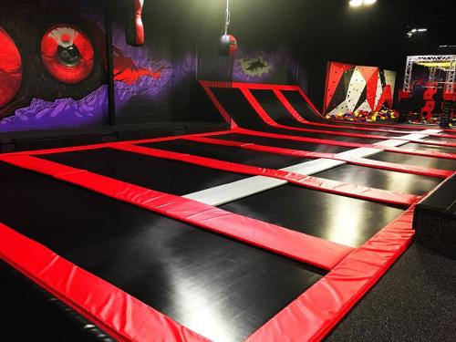 A vibrant indoor trampoline park featuring red and black trampolines and colorful wall art.