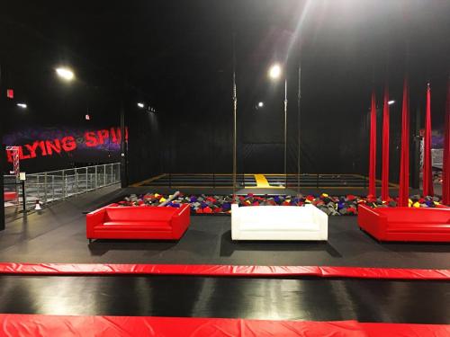 Interior of a trampoline park featuring colorful foam pits, red and white seating, and a black wall with "Flying Spin" text.