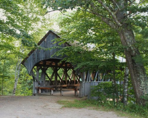 A rustic wooden covered bridge surrounded by lush green trees and foliage.