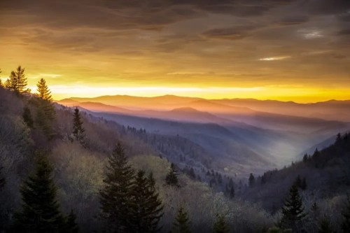 A serene mountain landscape at sunset, with layers of hills and a colorful sky filled with clouds.