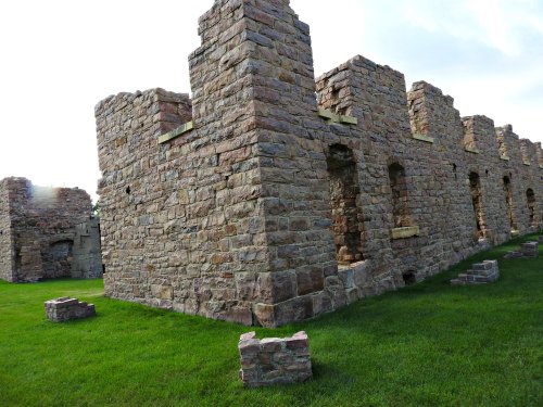 Stone ruins of a historic building, featuring weathered walls and grassy surroundings under a cloudy sky.