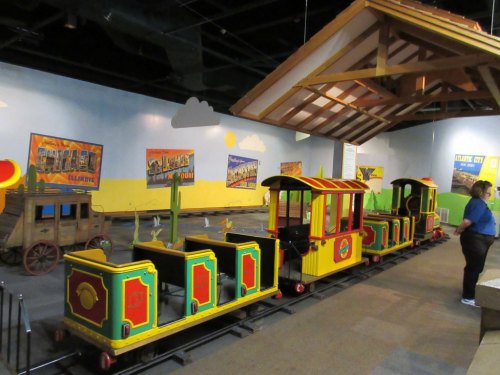 Colorful miniature train set in a themed indoor space, with a wooden structure and vibrant wall murals in the background.