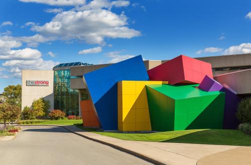 Colorful geometric shapes adorn the exterior of The Strong museum, set against a blue sky with fluffy clouds.