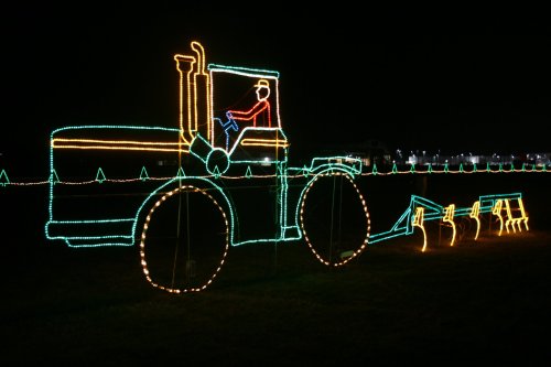 A brightly lit tractor made of string lights, with a figure in the driver's seat, set against a dark night sky.