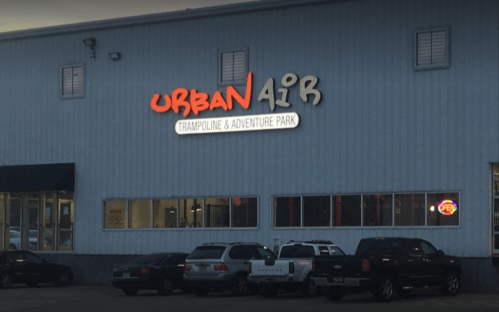 Sign for Urban Air Trampoline & Adventure Park on a building exterior, with parked cars in front.