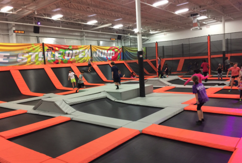 A vibrant indoor trampoline park with multiple trampolines and people jumping and playing.