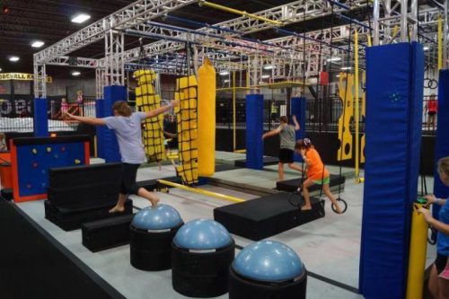 A vibrant indoor obstacle course with kids navigating various challenges like balance beams and climbing structures.