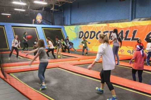 A lively indoor trampoline park with people playing dodgeball on trampolines, surrounded by colorful walls.