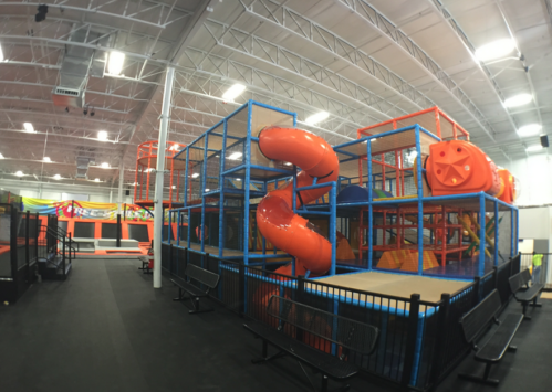 Indoor trampoline park featuring colorful play structures, slides, and safety barriers.