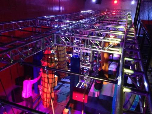 A colorful indoor obstacle course with metal structures, ropes, and climbing elements under vibrant lighting.