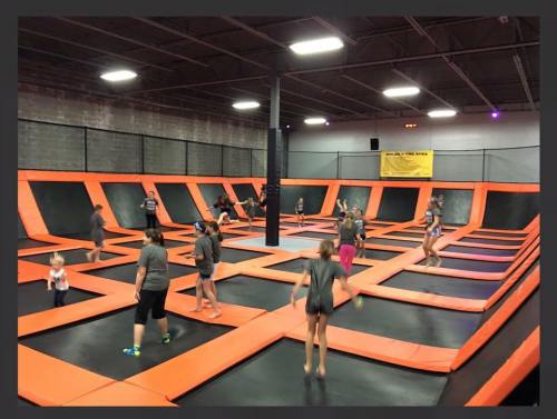 A lively indoor trampoline park filled with children jumping on orange and black trampolines.