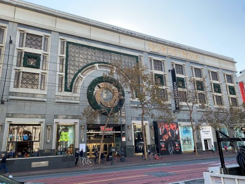 Exterior of a Nordstrom store with decorative elements, trees, and people walking by in an urban setting.