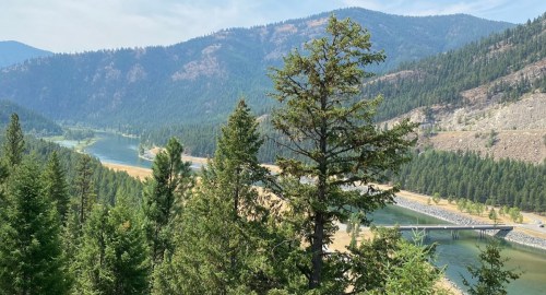 A scenic view of a river winding through a forested valley, surrounded by mountains and greenery.