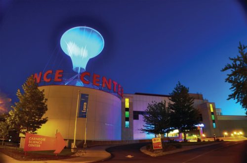 The Carnegie Science Center illuminated at night, featuring a large glowing light bulb above the entrance.