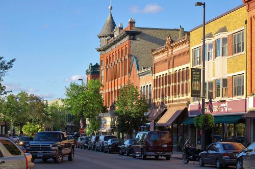 A charming downtown street lined with historic brick buildings and parked cars under a clear blue sky.