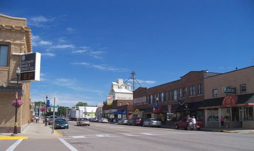 A sunny street view of a small town with shops, parked cars, and a clear blue sky.
