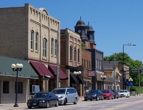 A charming street scene featuring historic buildings, shops, and parked cars under a clear blue sky.