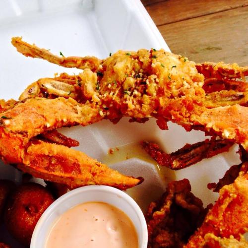 A close-up of a fried crab on a takeout container, accompanied by a small bowl of dipping sauce.
