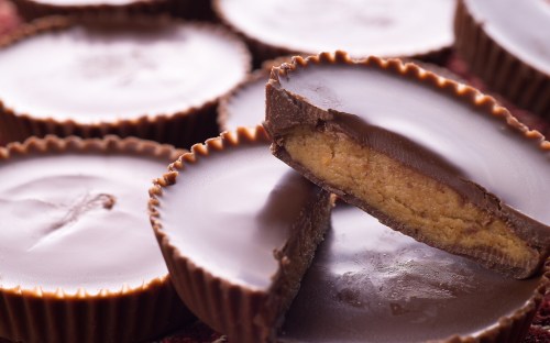 Close-up of chocolate cups with creamy peanut butter filling, some whole and one cut in half, revealing the filling.