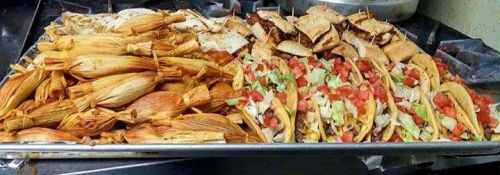 A tray of delicious Mexican food featuring tamales, tacos, and quesadillas, garnished with lettuce and tomatoes.