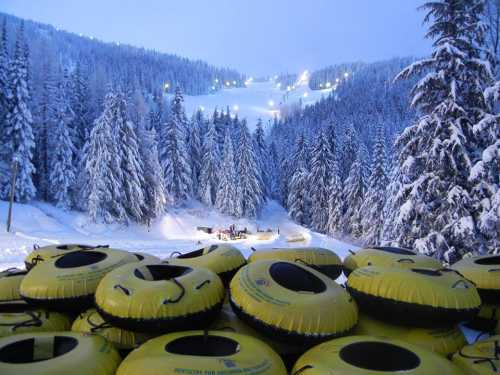 A stack of yellow snow tubes in the foreground, with a snowy mountain slope and trees in the background at dusk.